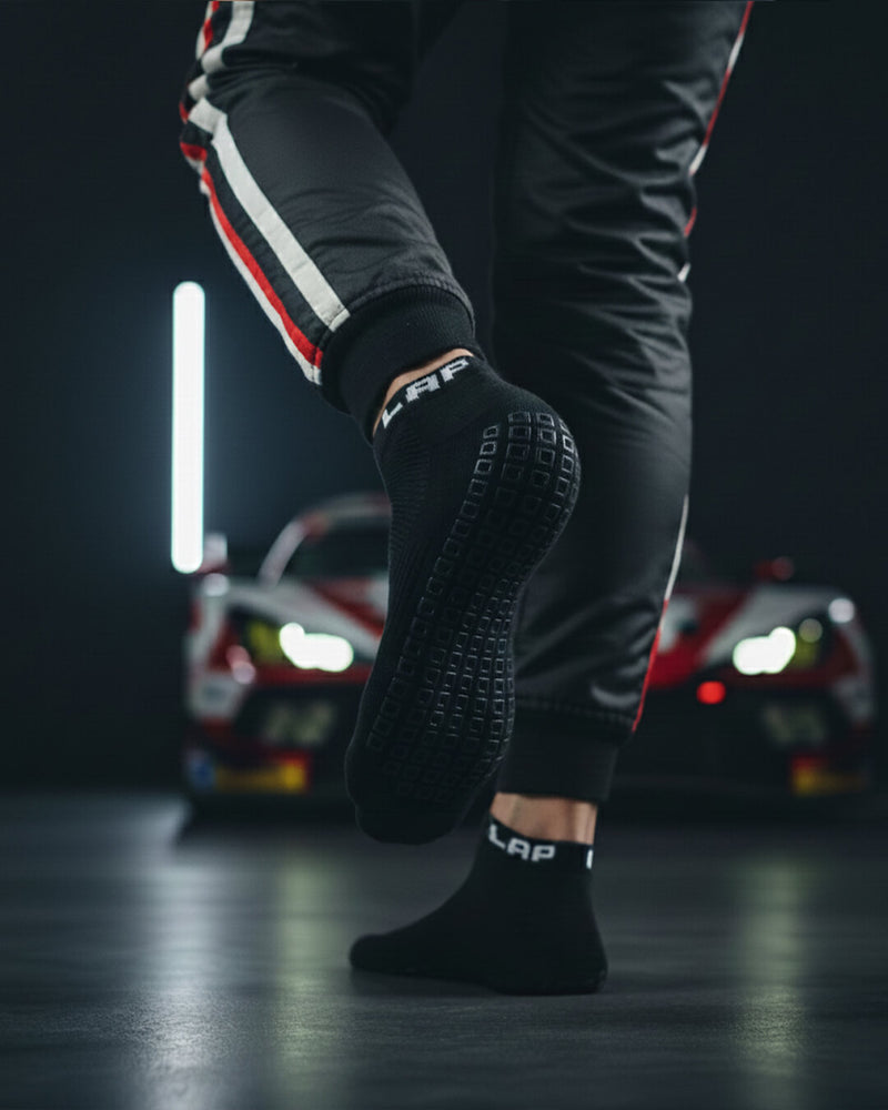 NitroGrip Obsidian socks sim racer lifting foot to view grippy sole with gt3 car in background